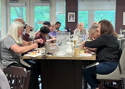 A group of guests at Hope Lodge Boston sit around a table, enjoying a meal served by the PTP Gives Back and AWS MASS SMB teams, sharing conversation and camaraderie.