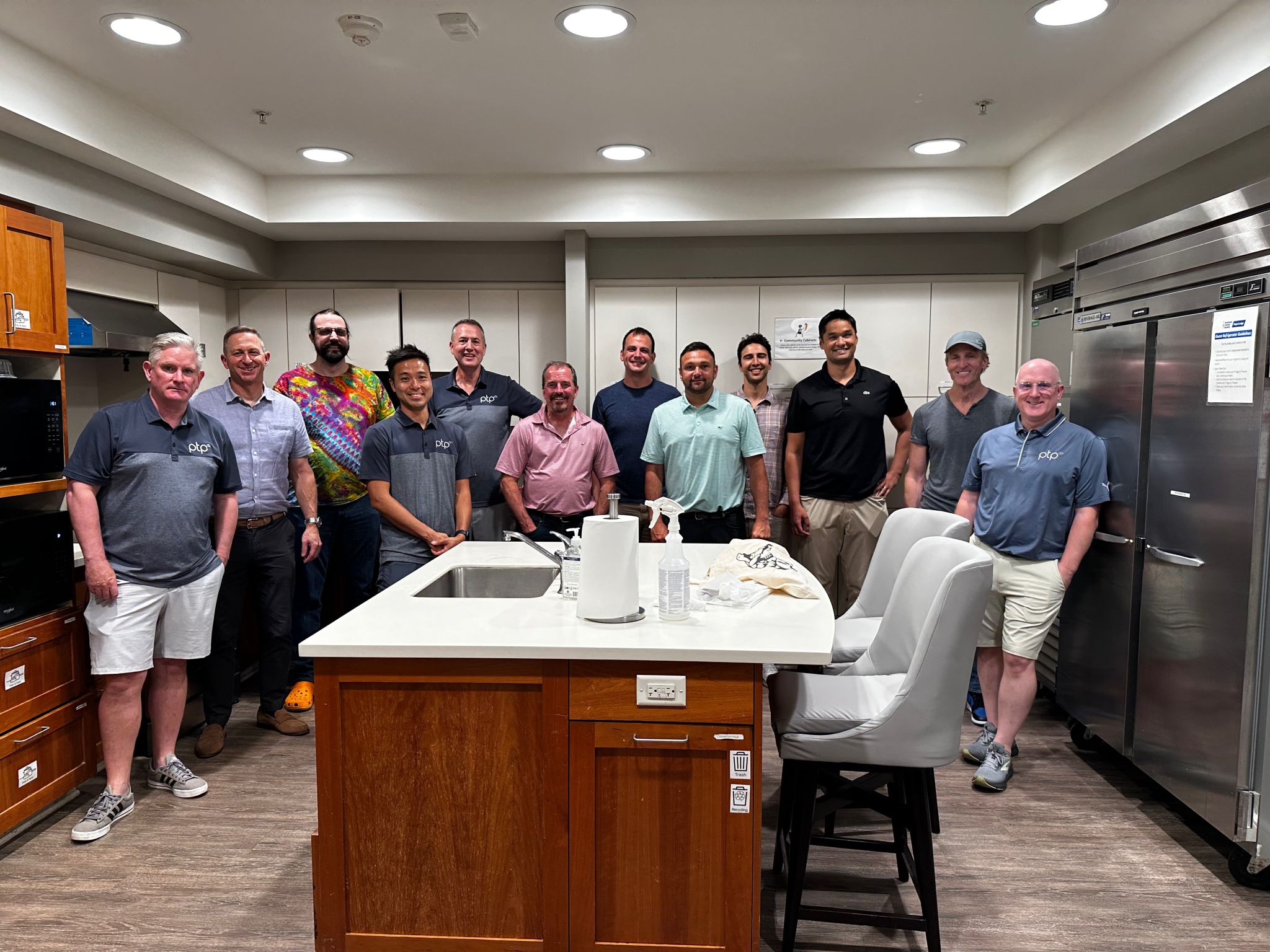 A group of volunteers from the PTP Gives Back team and the AWS MASS SMB team stand together in the kitchen of Hope Lodge Boston, smiling after serving a meal to cancer patients and their caregivers.