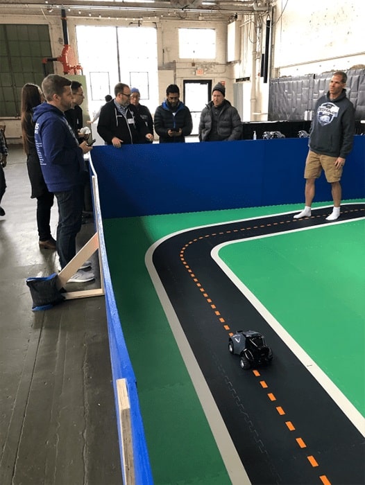 Attendees observing a demonstration at the AWS DeepRacer training event, featuring a large model racetrack.