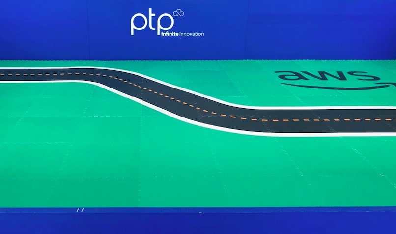 A miniature racetrack branded with PTP and AWS logos, symbolizing a collaboration at the AWS DeepRacer event.