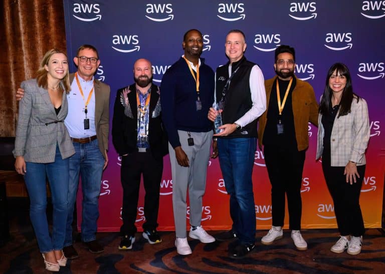 A group photo of PTP team members and AWS representatives at AWS re:Invent 2024, with Ethan Simmons holding an award.