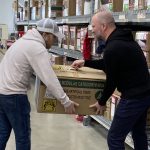 Micah and Nolan from the PeakPlus team collaboratively lifting a heavy box during a charity event at Matthew 25: Ministries.